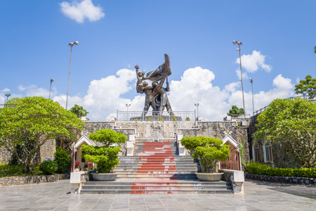 Dien Bien Phu, Vietnam - September 5, 2022: The image shows the Victory Monument featuring a large bronze statue of three figures holding a flag, situated at the top of a wide staircase with potted trees and landscaped greenery under a clear blue sky.のeditorial素材
