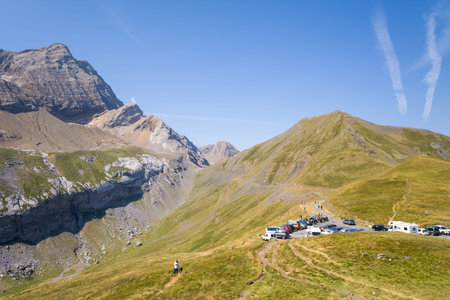 Parking dans les montagnes des Pyrenees, France - August 7, 2022: A parking area with several cars, vans, and people is visible on a grassy mountain ridge surrounded by high peaks under a clear blue sky.のeditorial素材