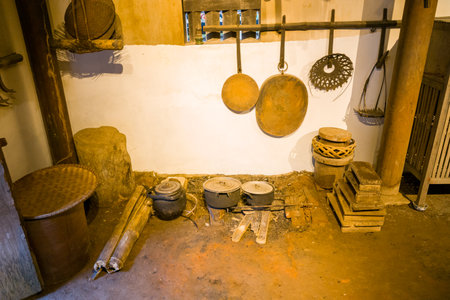 Hanoi, Vietnam - September 15, 2022: A traditional Vietnamese kitchen area is displayed at the Museum of Ethnology, showing cooking pots on an earthen floor, wooden utensils hanging on the wall, woven baskets, wooden blocks, and storage containers.のeditorial素材
