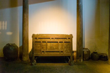 Hanoi, Vietnam - September 15, 2022: A traditional wooden chest is displayed between wooden pillars inside a Vietnamese house at the Museum of Ethnology, with several ceramic jars placed along the wall on an earthen floor.のeditorial素材
