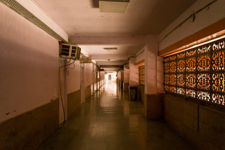 Delhi, India - March 14, 2022: Interior view of an empty corridor with polished floors, patterned metal window grilles on the right, air conditioning unit, fluorescent ceiling lights, and signage in Hindi in a public building.のeditorial素材
