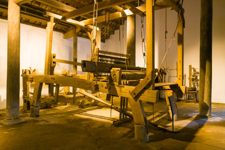 Hanoi, Vietnam - September 15, 2022: A large traditional wooden loom is exhibited between wooden pillars inside a Vietnamese house at the Museum of Ethnology, with beams, pulleys, and weaving components visible on an earthen floor.のeditorial素材