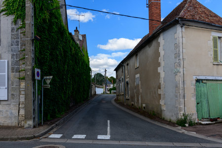 Pouilly sur Loire, France - June 27, 2022: A narrow street lined with residential buildings, one covered in green ivy, with a no parking sign, overhead wires, and partly cloudy sky.のeditorial素材