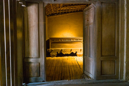 Hanoi, Vietnam - September 15, 2022: The interior of a traditional Cham house is shown with wooden doors open to reveal a carved wooden bed, bamboo flooring, and a thatched roof structure at the Museum of Ethnology.のeditorial素材