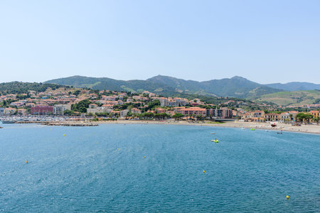 Unknown location - June 19, 2022: The image shows the waterfront of Banyuls-sur-Mer with a marina, residential buildings, and hills in the background under a clear sky.のeditorial素材