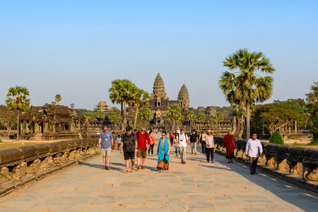 Angkor Wat, Cambodia - February 13, 2020: People are seen walking on the stone causeway lined with palm trees leading to the central towers of Angkor Wat under a clear blue sky.のeditorial素材