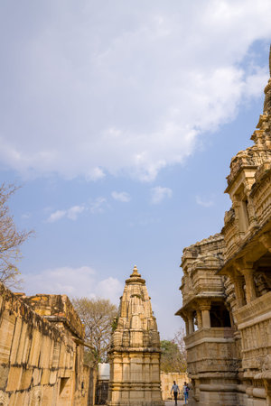 Chittorgarh, India - March 21, 2022: The image shows the central shikhara and surrounding carved stone buildings of Kumbhshyam Temple, with two people walking in the courtyard under a partly cloudy sky.のeditorial素材