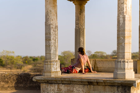 Chittorgarh, India - March 21, 2022: A person sits on the stone floor of an open pavilion with columns at Palace Maharani Padmini, looking out towards the landscape with trees and dry vegetation visible in the background.のeditorial素材