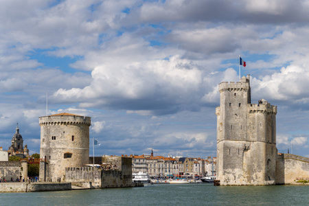 La Rochelle, France - August 31, 2020: The Saint Nicolas Tower and the Chain Tower, two historic stone fortifications, are visible on the waterfront at the entrance to the old port, with the French flag flying and residential buildings in the background uのeditorial素材