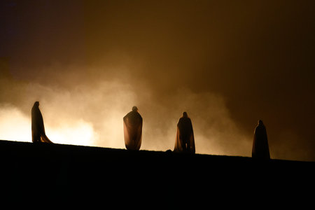 Unknown location - July 17, 2021: Four people wearing cloaks are silhouetted against bright stage lighting and smoke during a nighttime outdoor performance.のeditorial素材