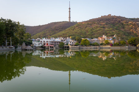 Bundi, India - March 20, 2022: Nawal Sagar Lake is seen with reflections of city buildings, trees, a hillside, and a prominent telecommunications tower under a clear sky.のeditorial素材