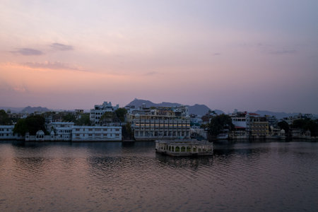 Udaipur, India - March 23, 2022: Historic waterfront buildings and the Gangaur Ghat pavilion are visible on the edge of Lake Pichola at dusk, with mountains in the background and a pastel sky overhead.のeditorial素材