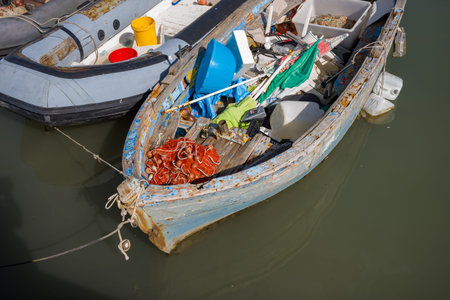 Trani, Italy - October 16, 2020: An old wooden fishing boat with peeling paint is moored in the water, filled with fishing nets, plastic containers, and various fishing equipment.のeditorial素材