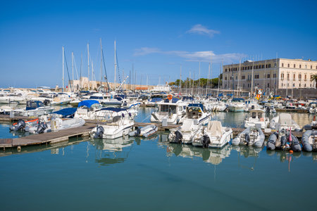 Trani, Italy - October 16, 2020: The image shows a marina filled with various boats and yachts docked at piers, with a large historic building and clear blue sky in the background.のeditorial素材