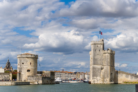 La Rochelle, France - August 31, 2020: The Saint Nicolas Tower and the Chain Tower, two historic stone fortifications, are visible on the waterfront at the entrance to the old port, with the French flag flying and residential buildings in the background uのeditorial素材