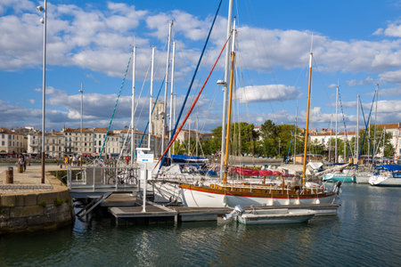 La Rochelle, France - September 1, 2020: Several sailboats are moored at a marina with a floating dock, bicycles, and people walking along the quay, with rows of historic waterfront buildings and a prominent clock tower visible in the background under a pのeditorial素材
