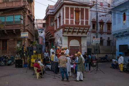 Jodhpur, India - March 25, 2022: The image shows a group of musicians with microphones, speakers, and instruments preparing for a street concert in a residential area with traditional blue and red-painted buildings, utility wires overhead, and people gathのeditorial素材