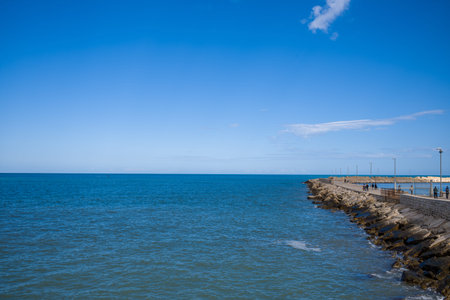 Trani, Italy - October 16, 2020: Several people are visible walking along a long stone pier that extends into the Adriatic Sea under a clear blue sky.のeditorial素材