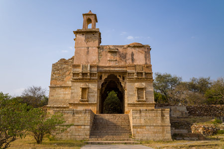 Chittorgarh, India - March 21, 2022: The image shows the ruins of an ancient stone gateway with steps leading up to the entrance at Place Johar, featuring weathered walls, partial upper structure, and surrounding vegetation under a clear sky.のeditorial素材