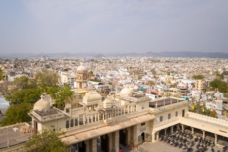 Udaipur, India - March 24, 2022: Elevated view showing the ornate domes and architecture of City Palace in the foreground with the densely built old city of Udaipur and surrounding hills in the background.のeditorial素材