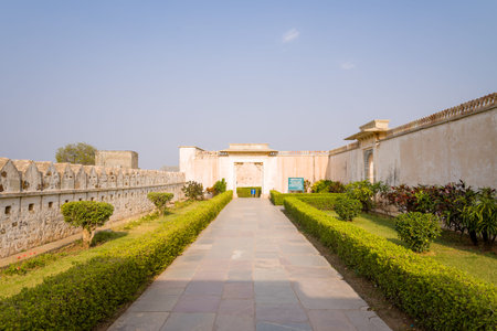 Chittorgarh, India - March 21, 2022: A stone pathway bordered by manicured hedges and shrubs leads to the entrance of Palace Maharani Padmini, with high stone walls and a clear sky visible in the background.のeditorial素材