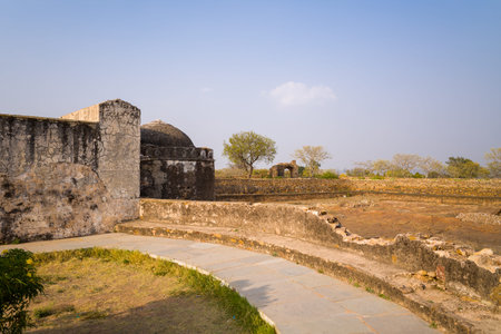Chittorgarh, India - March 21, 2022: A curved stone walkway leads past a weathered stone wall and...