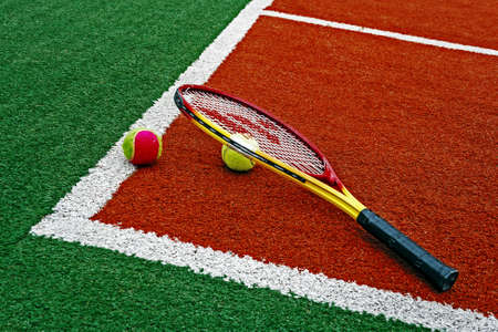 Colored tennis balls and rackets, placed in the corner of a synthetic field の写真素材
