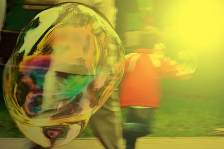 Child playing with bubble blower in sunset light. Giant bubbles, launched at International...