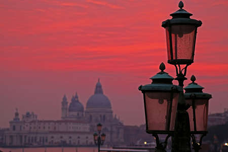 Sunset red and lanterns lit street in Venice, Italy, with Santa Maria della Salute church on background.の写真素材