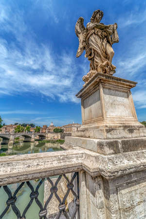 ROME, ITALY - JUNE 1, 2017: Statue of Agnel from Angel's Bridge by sculptor Ercole Ferrata, in front of castle San Angelo. Vatican Basilica in background.のeditorial素材