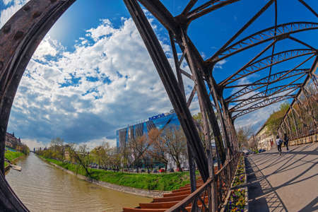 TIMISOARA, ROMANIA - APRIL 10, 2018: Old and new together in Timisoara. The modernist NOKIA building seen from an old pedestal metal bridge designed by Gustave Eiffel and a view along the Bega River.のeditorial素材