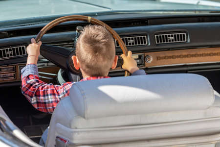 Funny image with one little boy at the wheel of an old and vintage car.の写真素材