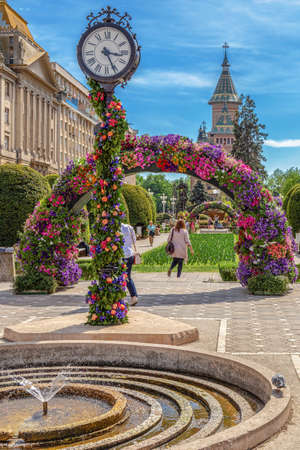 TIMISOARA, ROMANIA - APRIL 27, 2018: Beautiful floral decorations in Victory Square with old clock in foreground and Metropolitan cathedral in background. Flower Festival organized by the City Hall.のeditorial素材