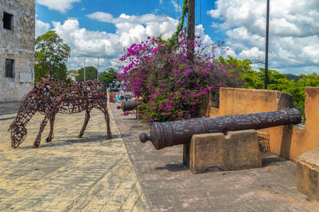 SANTO DOMINGO, DOMINICAN REPUBLIC - MARCH 13, 2020: Sculpture of an iron horse in front of the Royal Houses museum building and near famous Sundial. Modern art. Medieval cannon and defense walls.のeditorial素材