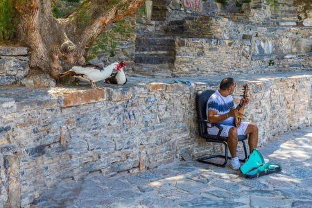 Agios Nikolaos, Crete, Greece - July 24, 2021: Funny street singer with twoo dancer birds at Lake Voulismeni, with bouzouki also spelled buzuki or buzuci, a musical instrument popular in Greece.のeditorial素材