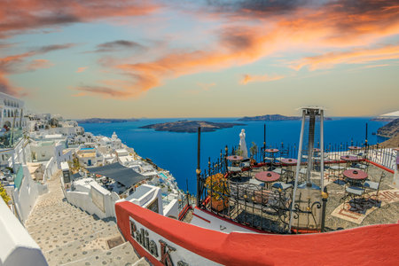 FIRA (Thira), SANTORINI, GREECE - JUNE 21, 2021: Typical white architecture with restaurants and hotels at Fira, the capital of Santorini island. Volcanic island Nea Kameni in background.のeditorial素材