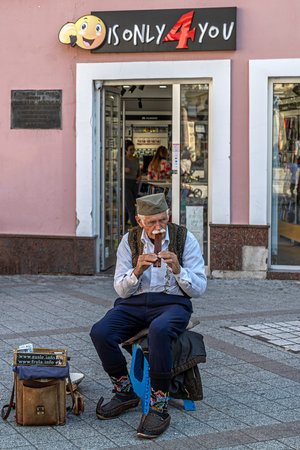 NOVI SAD, SERBIA - OCTOBER 14, 2023: Old man dressed in traditional Serbian clothes playing in the street a folk melody at one popular musical instrument, a double whistle.のeditorial素材