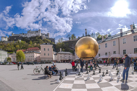 SALZBURG, AUSTRIA - APRIL 27, 2023: Chess game drawn on asphalt in Kapitelplatz, near monument to Paul Fuerst "Sphere", a golden ball on which stands a small man. Castle Hohensalzburg in background.のeditorial素材