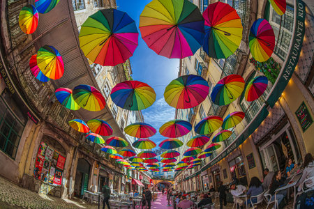LISBON, PORTUGAL - APRIL 7, 2024: The famous pedestrian Pink street of Rua Nova do Carvalho, Cais do Sodre area, with colorful rainbow umbrellas hanging between the buildings.のeditorial素材