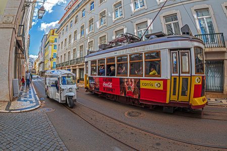 LISBON, PORTUGAL - APRIL 8, 2024: Touristic transport with funny electric car called Tuk Tuk and vintage tram on the city streets.のeditorial素材