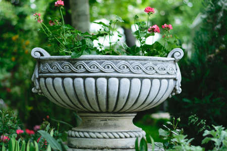decorative flower pot holder made from cement with red geranium flowersの写真素材