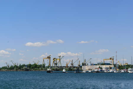 Mangalia, Constanta, Romania - July 7, 2017: boat anchored at the Mangalia civil harbor in Romania. In the background there are the heavy industry marine cranes from the Mangalia commercial harbor.のeditorial素材