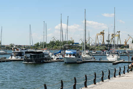 Mangalia, Constanta, Romania - July 7, 2017: boat anchored at the Mangalia civil harbor in Romania. In the background there are the heavy industry marine cranes from the Mangalia commercial harbor.のeditorial素材