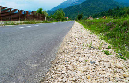 asphalt road with gravel on the side leading to the mountains in the far backgroundの写真素材