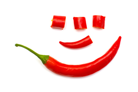 Red chili pepper cut into slices lined with a human face like a clown isolated on white background. Creative spicy sharp. Flat lay, top viewの写真素材
