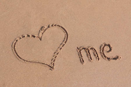 Love me written on  sand on a beach with heart symbol and word meの写真素材