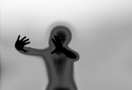 Silhouette of toddler behind textured glass wall with hands on itの写真素材