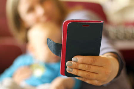 Mobile phone in mom's left hand while is making selfie with baby in the armsの写真素材