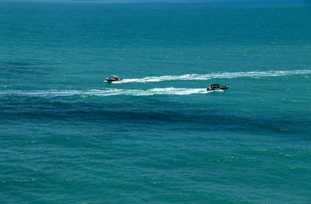Two speedboats with passengers sail on deep perfectly blue sea in the opposite directions leaving a white trail behindの写真素材