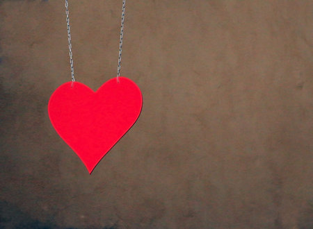 Hung with two chains red metal heart in front of the brown beige wall as a sign for loveの写真素材